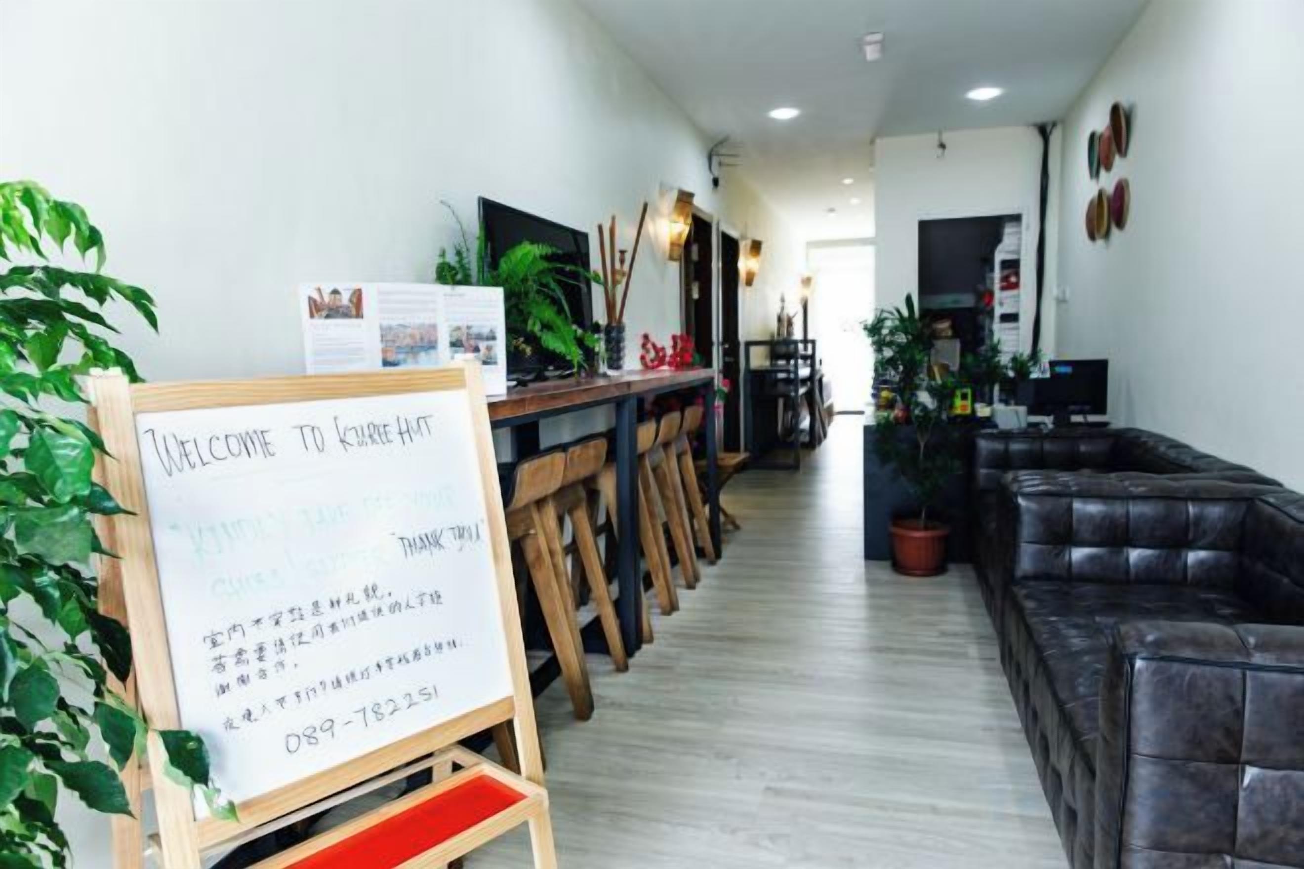 A reception area with a welcome sign, wooden chairs, a black leather sofa, and potted plants.