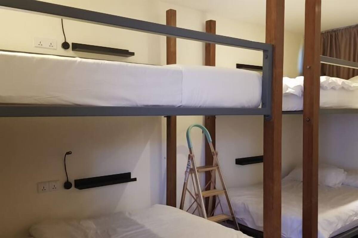 A bunk bed room with a ladder, a shelf, and a power outlet on the wall.