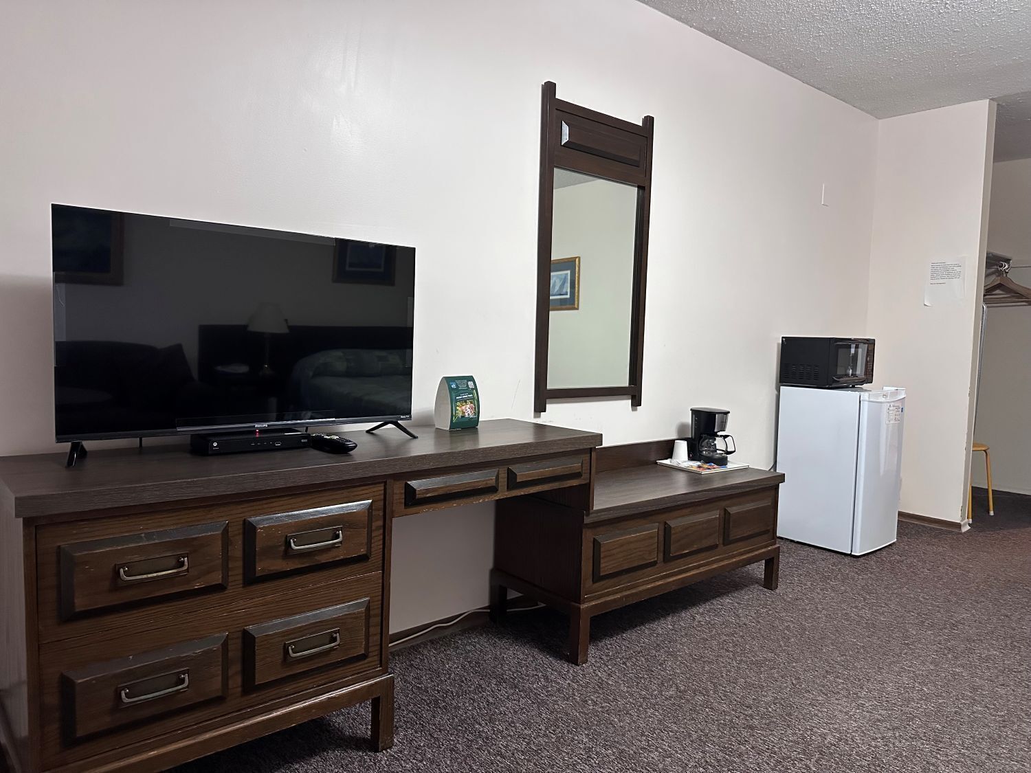Une chambre d’hôtel équipée d’un téléviseur à écran plat, d’une commode en bois avec des tiroirs, d’un four à micro-ondes et d’un réfrigérateur.