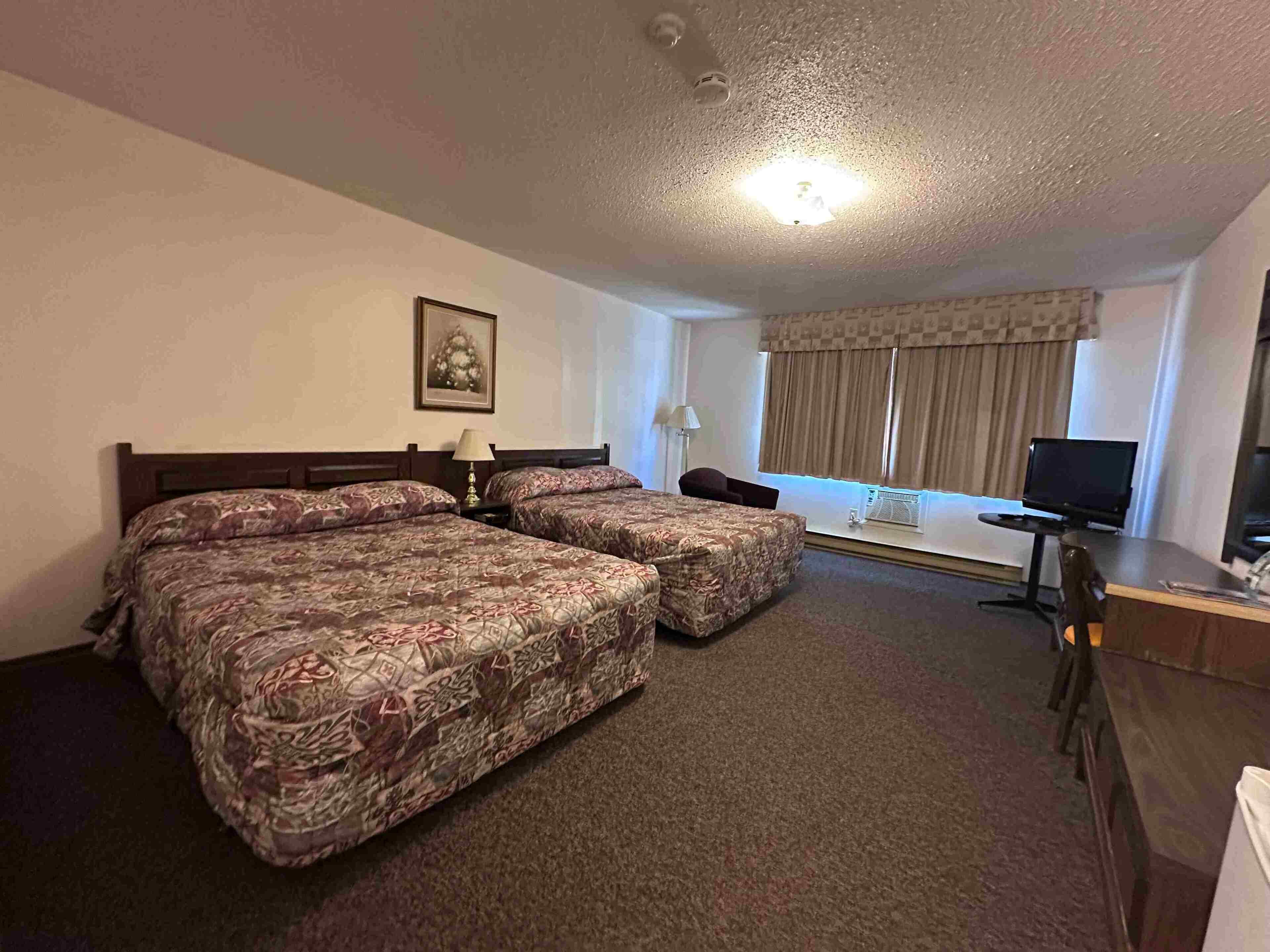 A hotel room with two beds, a desk, a television, and a window with curtains.