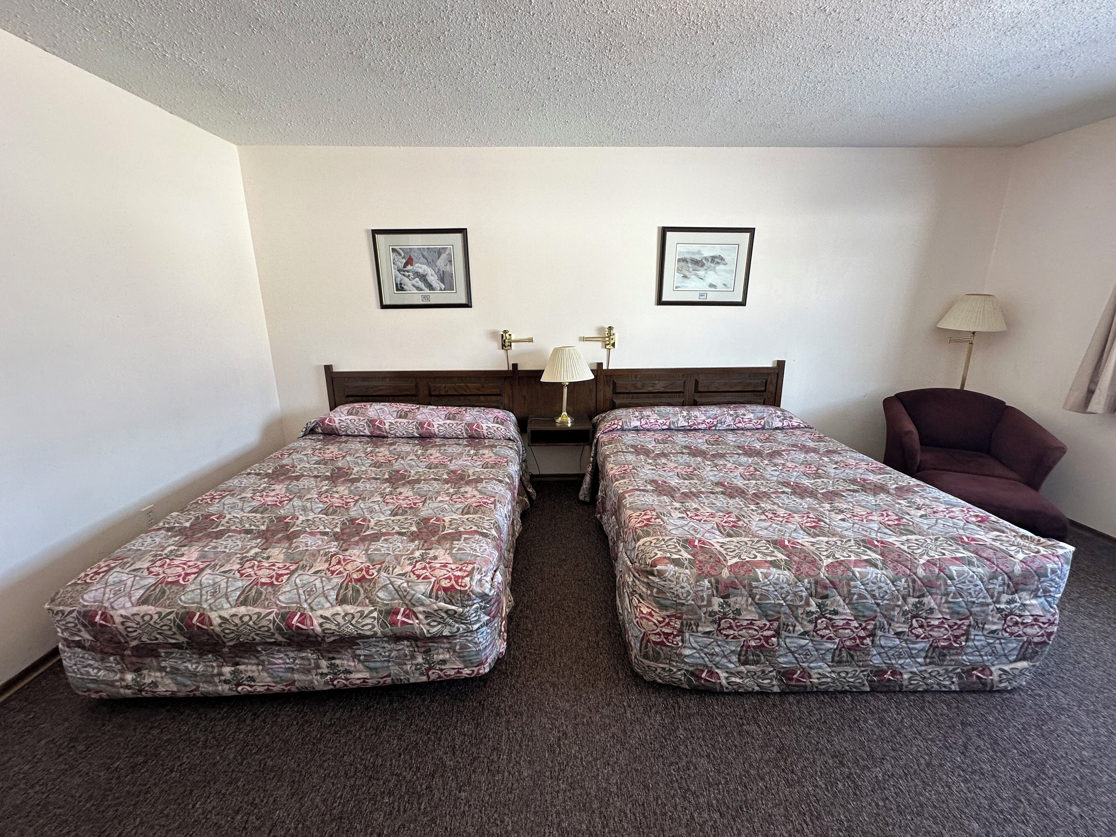 A twin room with two single beds, a wooden headboard, a desk with a lamp, and a chair.