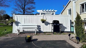 A backyard with a white fence, a bench, a grill, and a potted plant. - Auberge Eldo Inn (Blind River)