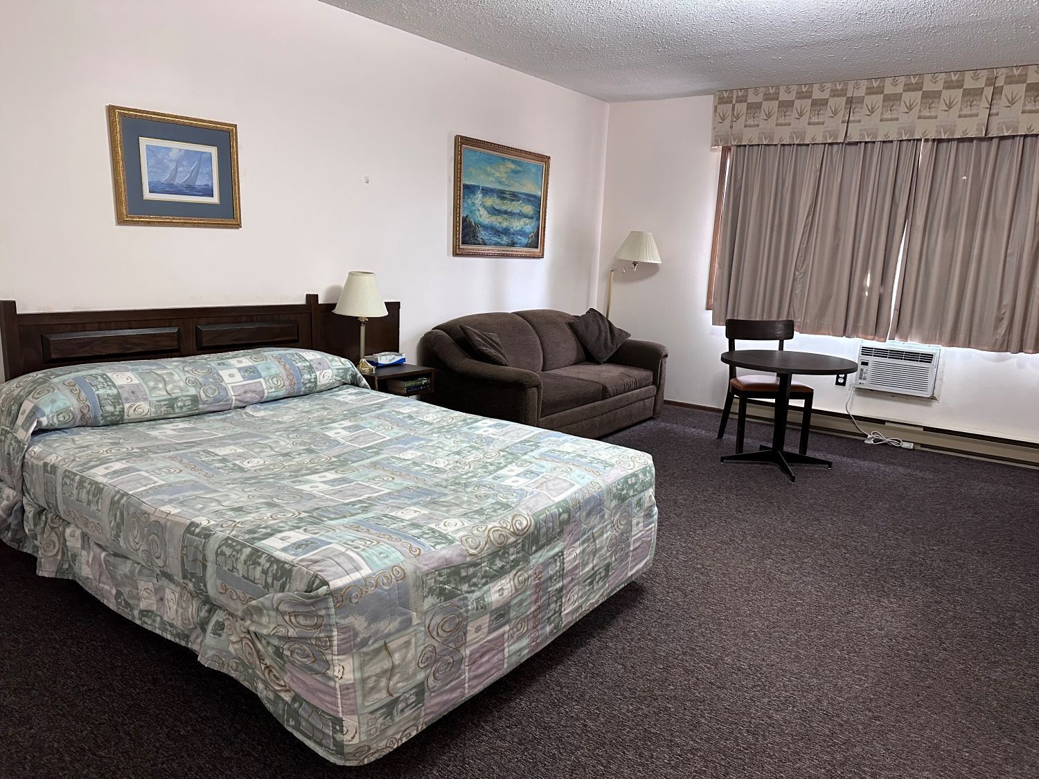 Une chambre d’hôtel avec un lit, un canapé, un bureau et deux tableaux accrochés au mur.