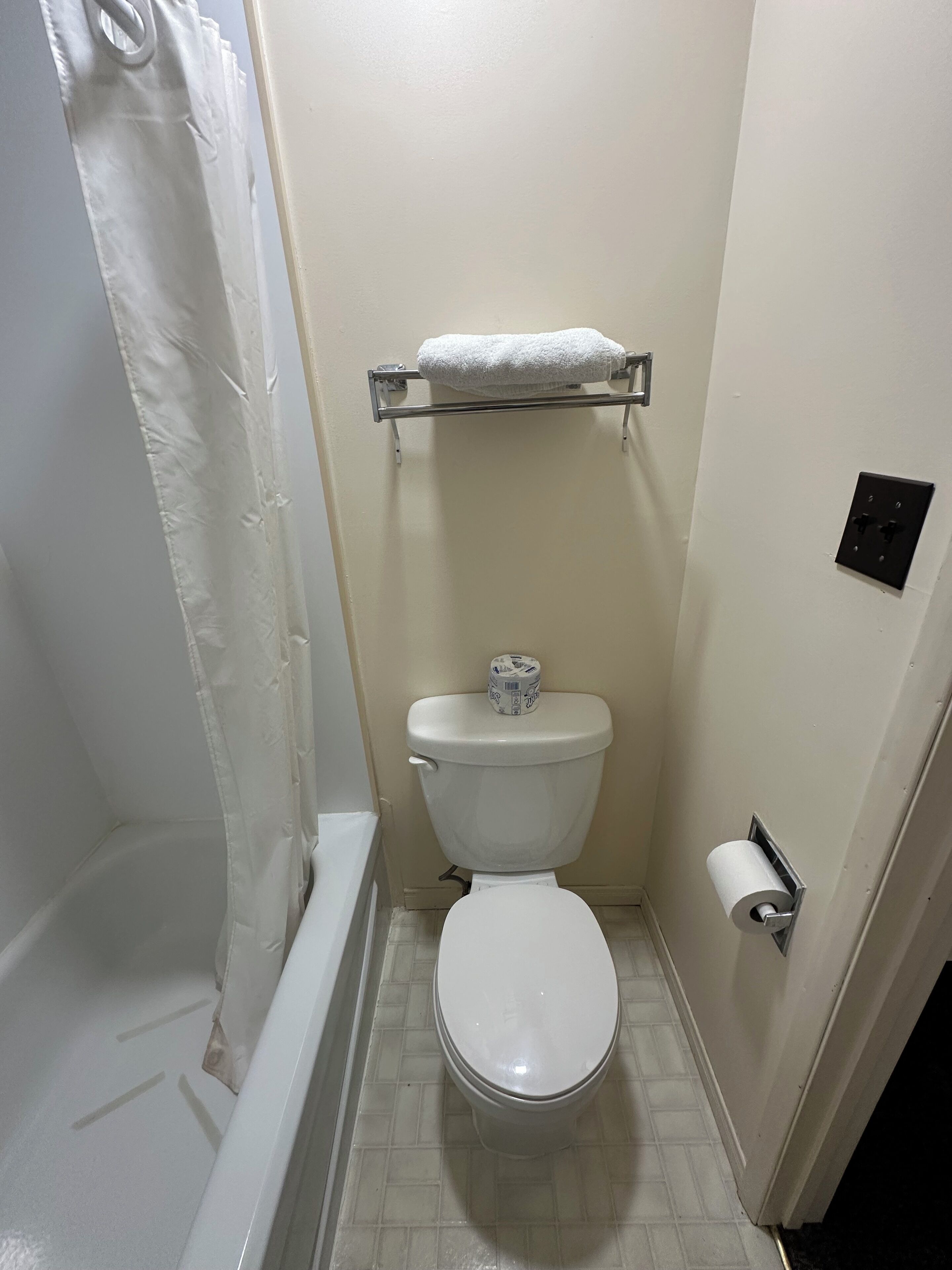 A small bathroom with a toilet, a shower curtain, a towel rack, and a toilet paper holder.