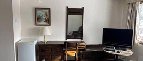 Habitación de hotel con escritorio, silla, televisión, cómoda y un cuadro en la pared.