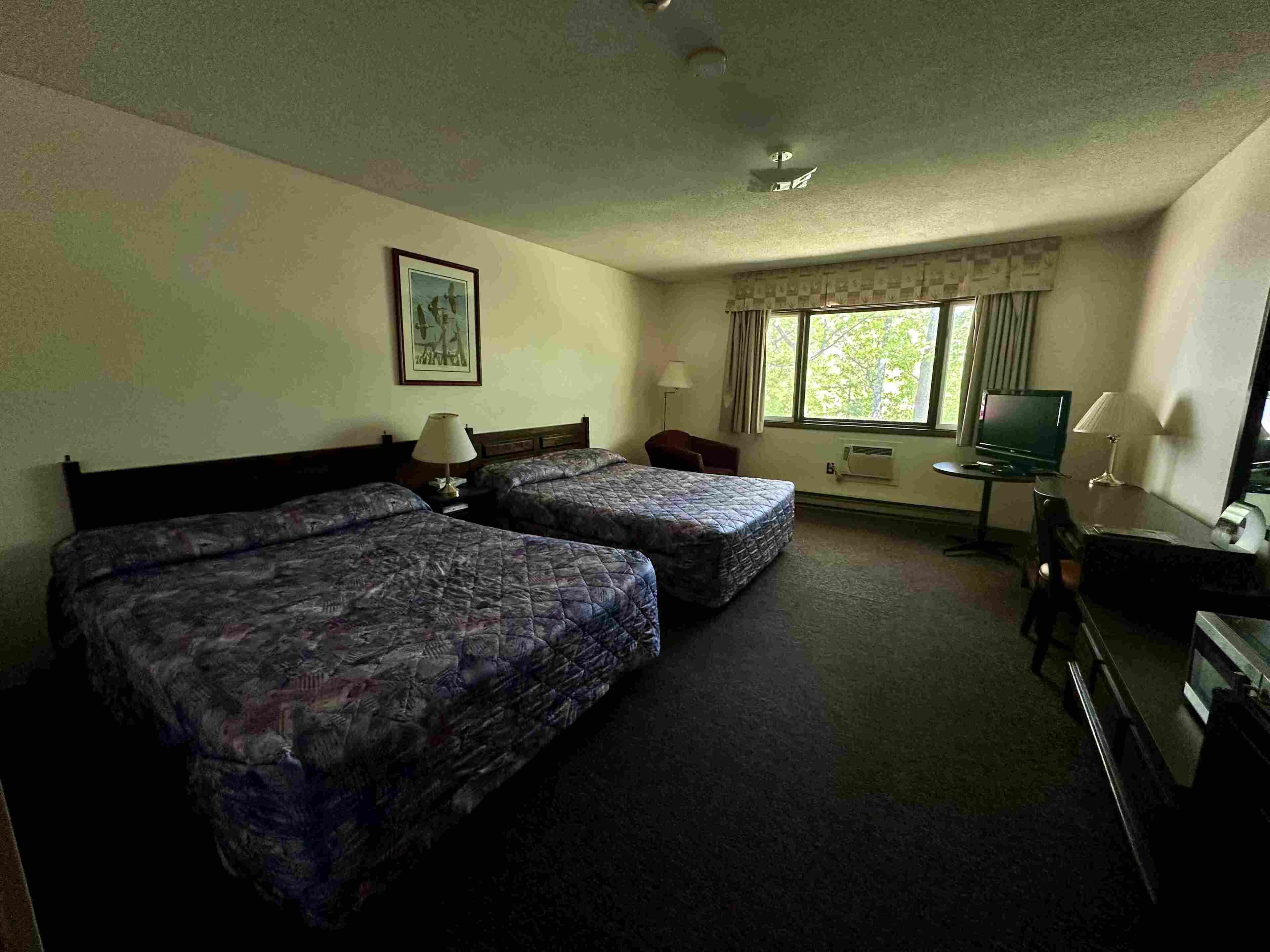 Una habitación de hotel con dos camas, un escritorio, un televisor y una ventana con cortinas.