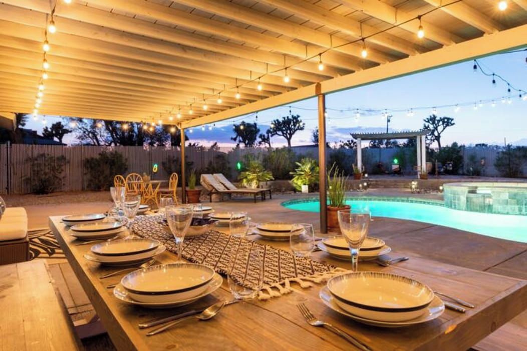 An outdoor dining area with a pool, string lights, and a wooden pergola.