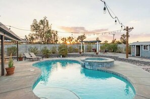 A swimming pool with a curved design, surrounded by a patio area with lounge chairs and potted plants.
