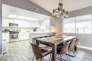 A modern kitchen with white cabinets, a central island, and a dining area with a wooden table and chairs.