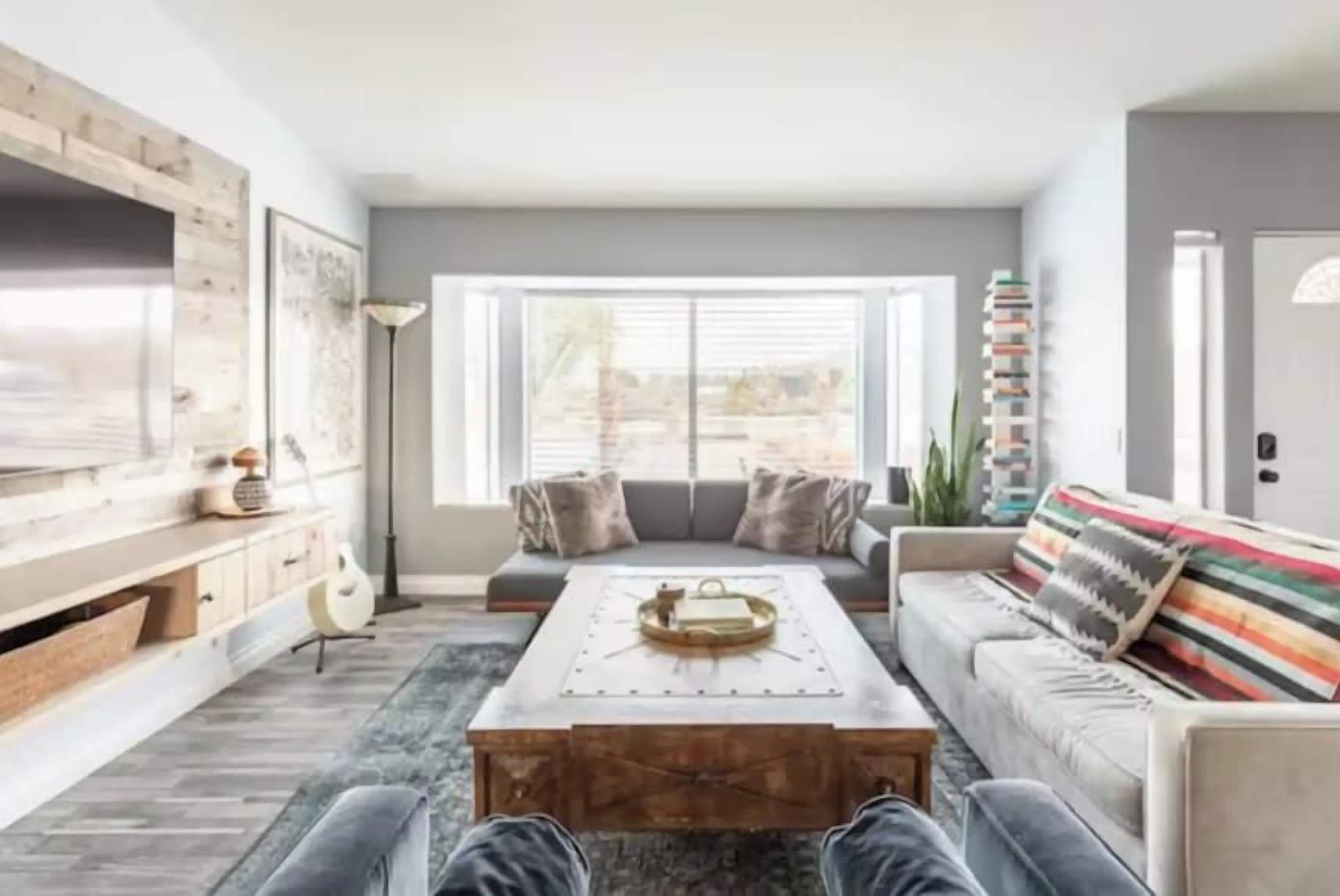 A modern living room with a large wooden coffee table, a sofa with colorful cushions, and a bookshelf.