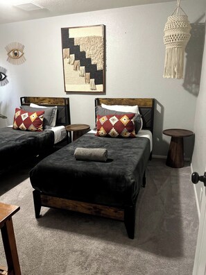 A hotel room with two beds, a small table, a wall-mounted macrame light, and a framed artwork. - Yucca Valley Oasis: Pool, Spa & Game Room Retreat (Yucca Valley)