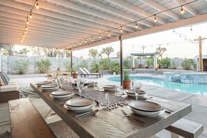 An outdoor dining area with a pool, covered seating, and string lights. - Yucca Valley Oasis: Pool, Spa & Game Room Retreat (Yucca Valley)