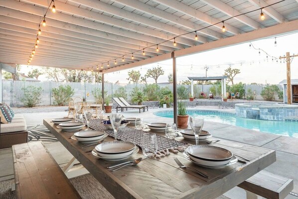 An outdoor dining area with a pool, covered seating, and string lights.