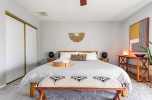 A bedroom with a bed, bedside tables, a wall-mounted fan, and a decorative wall piece.