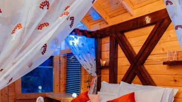 A cozy wooden cabin room with a bed, pillows, and a canopy.