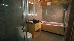 A bathroom with a wooden vanity, a glass shower enclosure, a marble-tiled wall, and a bathtub with rose petals.