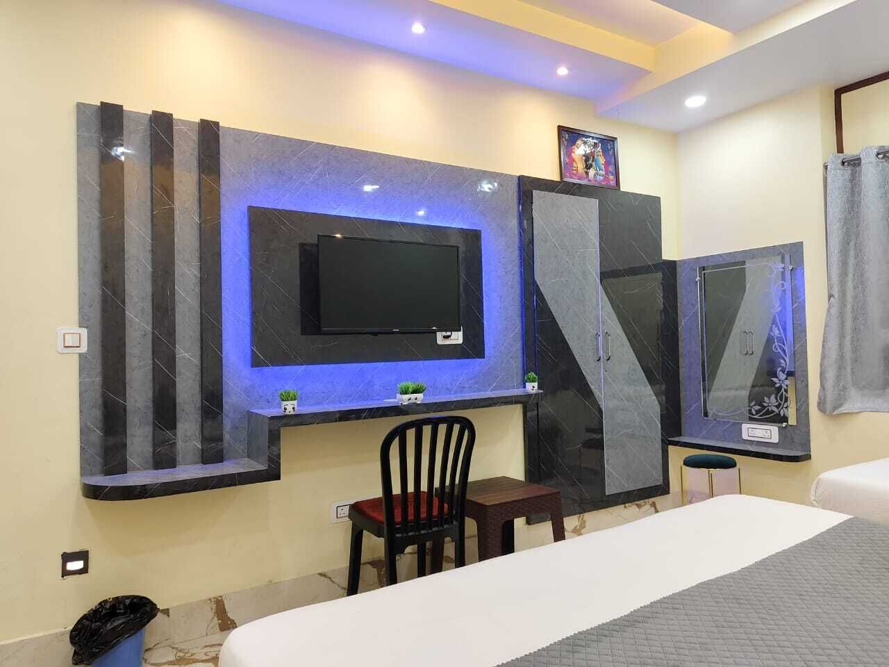 A hotel room with a bed, a desk with a chair, a TV mounted on the wall, and a mirror.