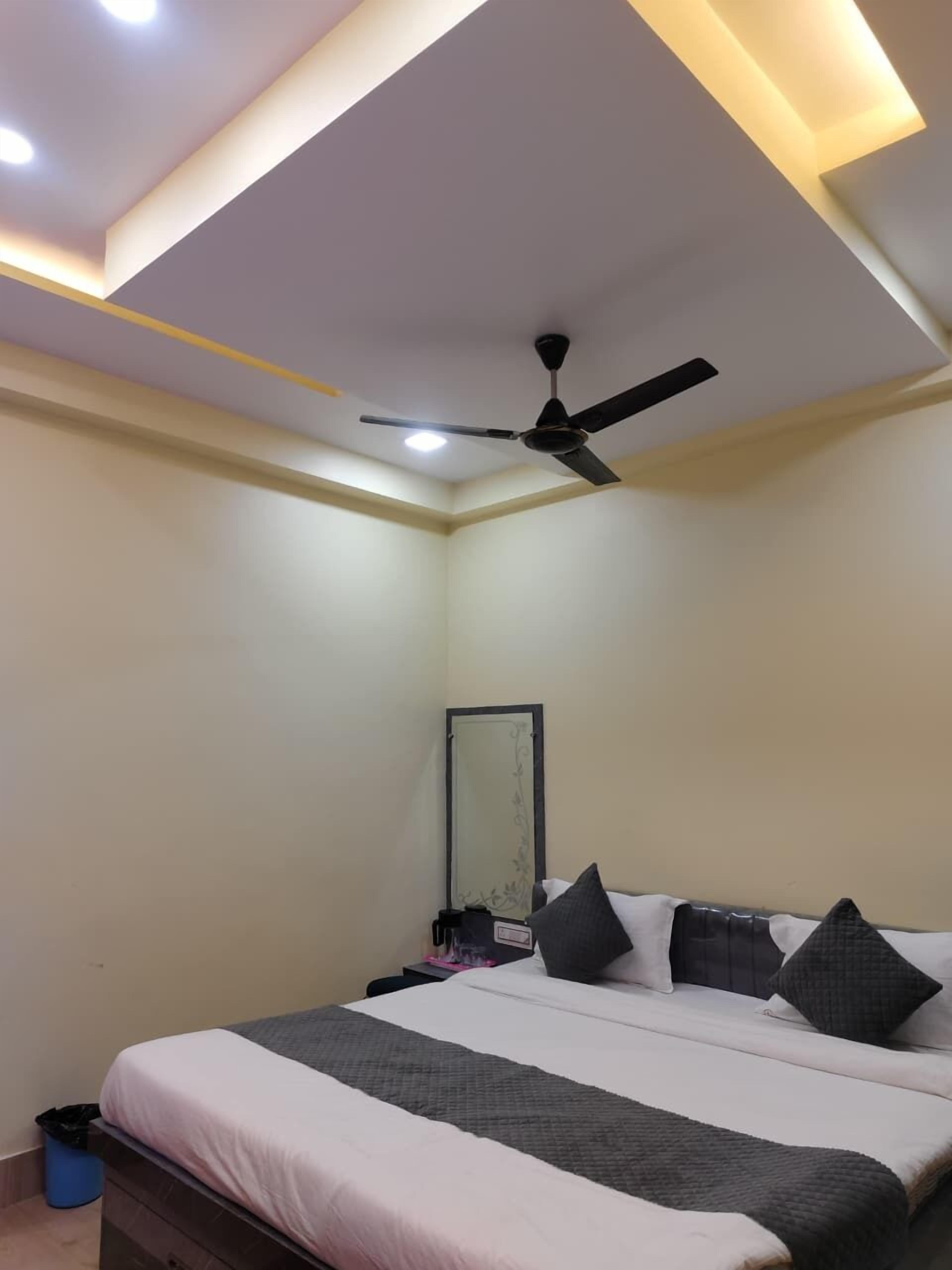 A bedroom with a bed, a ceiling fan, a mirror, and a trash bin.