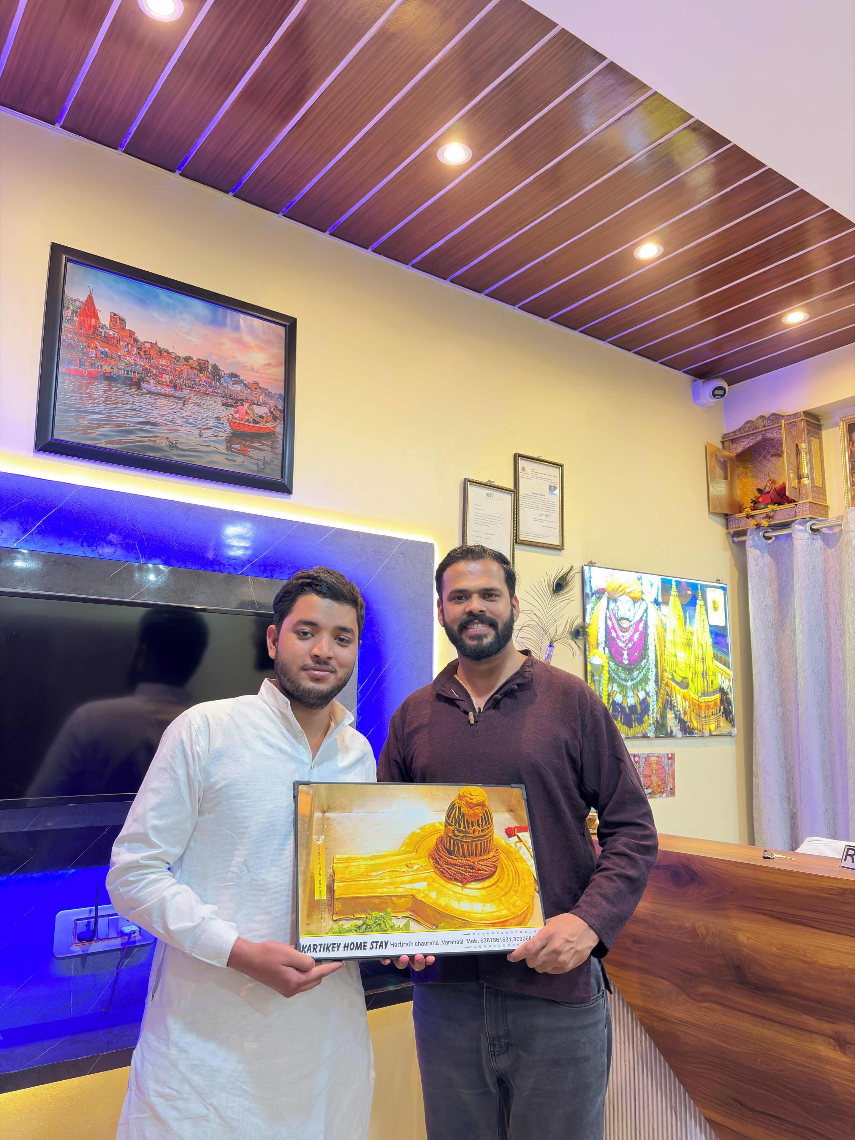 Uma área de recepção com teto de madeira, televisão, certificados emoldurados e uma pintura emoldurada de um templo.