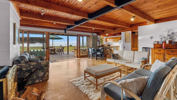 A spacious living area with a wooden ceiling, a large sofa, a coffee table, and a view of the outdoors. - Lakefront Retreat - Lake Taupo Holiday Home (Tauranga Taupo)