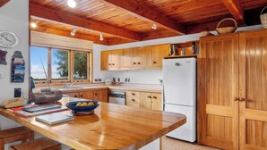 A kitchen with wooden cabinets, a white refrigerator, a wooden countertop, and a window with a view of trees. - Lakefront Retreat - Lake Taupo Holiday Home (Tauranga Taupo)