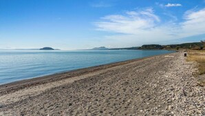 A pebbly beach with calm water and distant hills. - Lakefront Retreat - Lake Taupo Holiday Home (Tauranga Taupo)