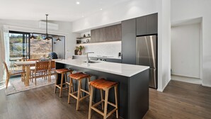 Eine moderne Küche mit Kochinsel, Barhocker, Kühlschrank und Essbereich mit Blick ins Freie.
