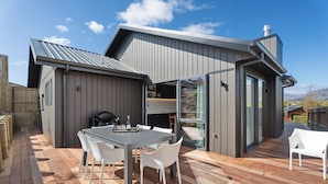 Ein modernes Haus mit einer Terrasse, einem Grill und einer Glasdoor, die auf eine Terrasse führt.