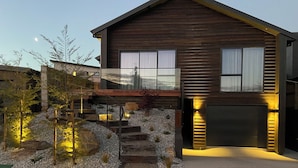 Ein modernes, zweistöckiges Haus mit Holzfassade, einer sichtbaren Garage und einem angelegten Vorgarten mit Treppe zum Eingang.