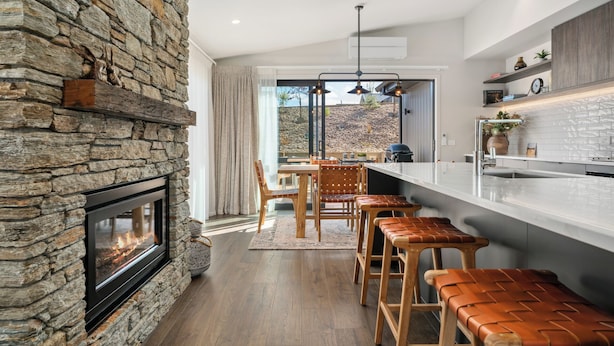 Eine moderne Küche mit Steinwand, Kamin, Barhocker und Blick ins Freie.