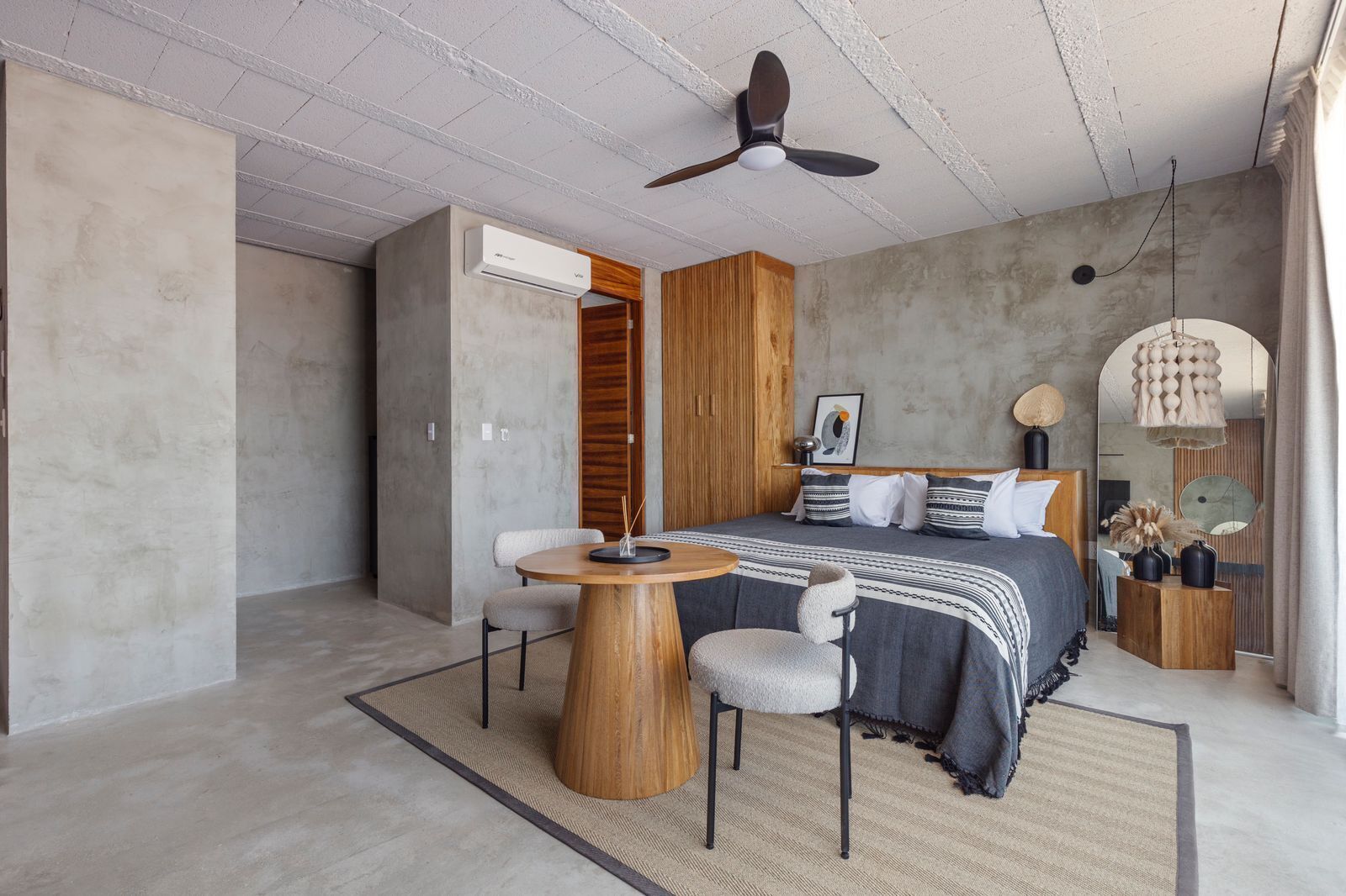 A modern bedroom with a bed, a wooden side table, a round wooden table, and a ceiling fan.