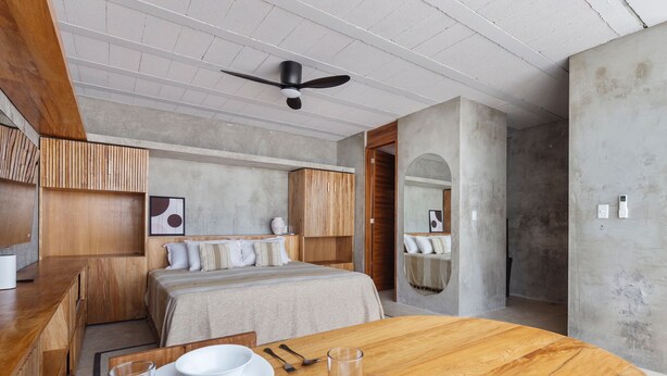 A modern bedroom with a wooden bed, a dining table with a bowl and utensils, and a ceiling fan. - #2 Down Town Loft with pool in the heart of Cancun (Cancún)