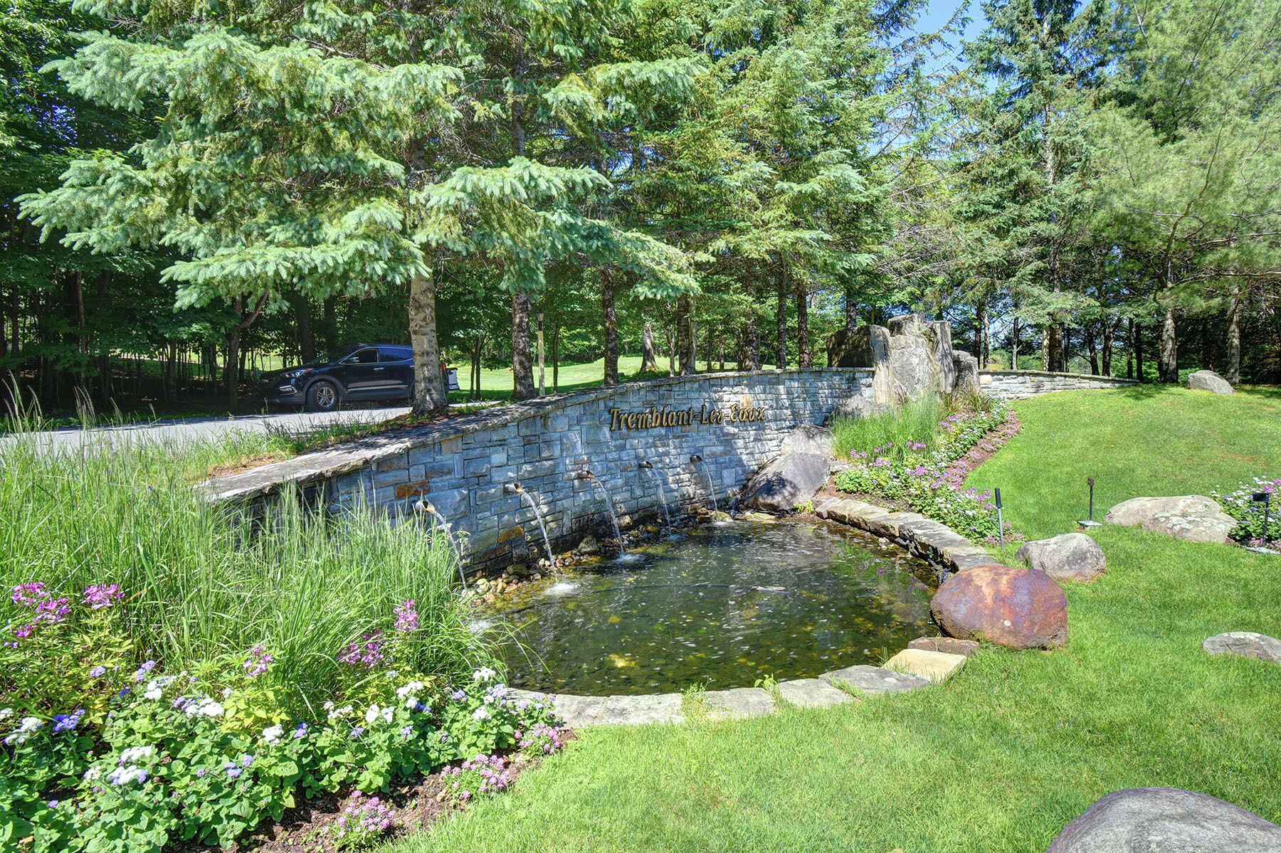 A stone wall with a pond, surrounded by grass and flowering plants.