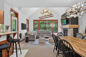 A modern interior with a dining area, sofa, fireplace, and large windows. - 205 Les Eaux Unit 7 (Mont-Tremblant)