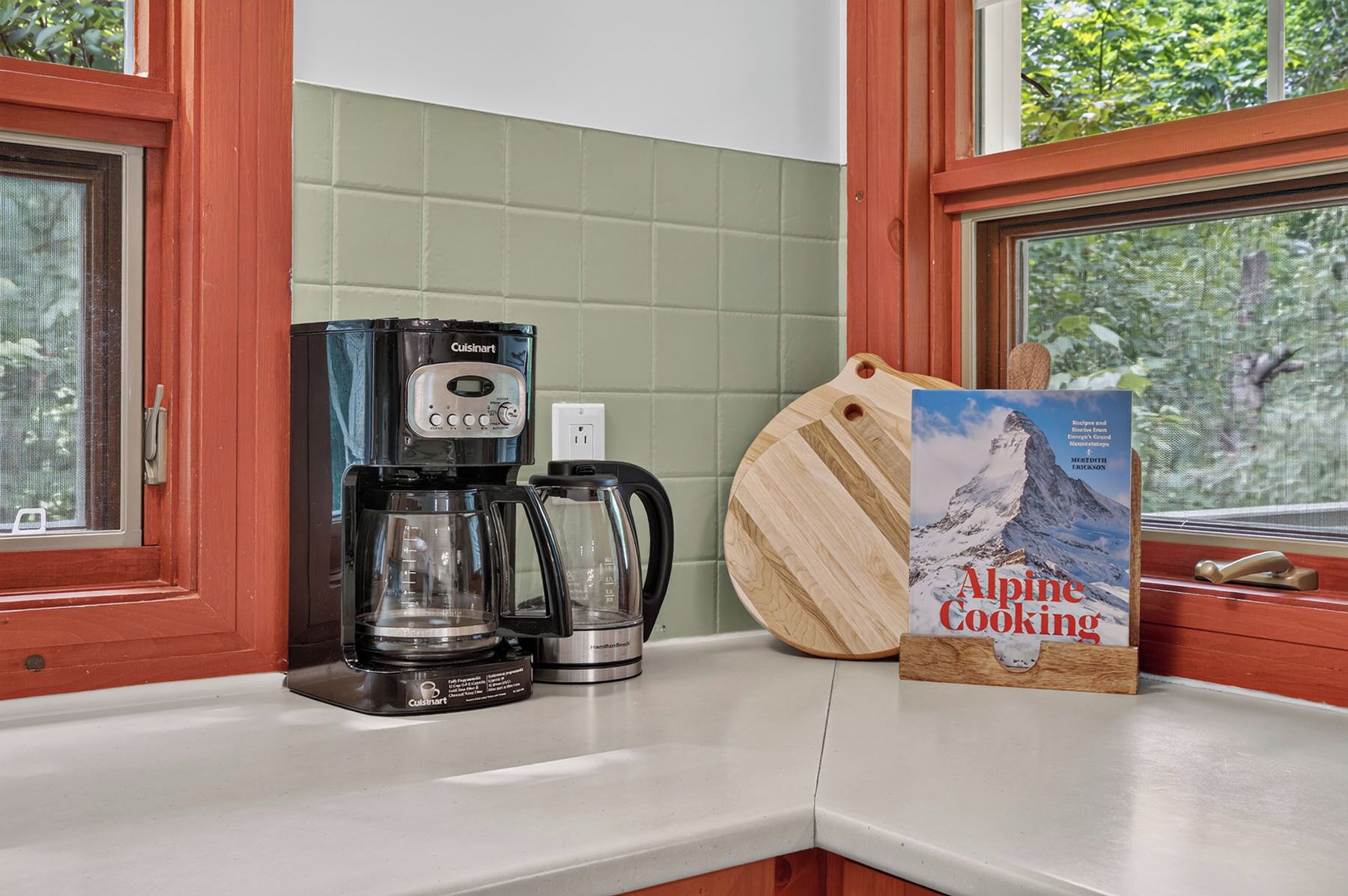 Una cocina con cafetera, hervidor y libro de cocina sobre la encimera.