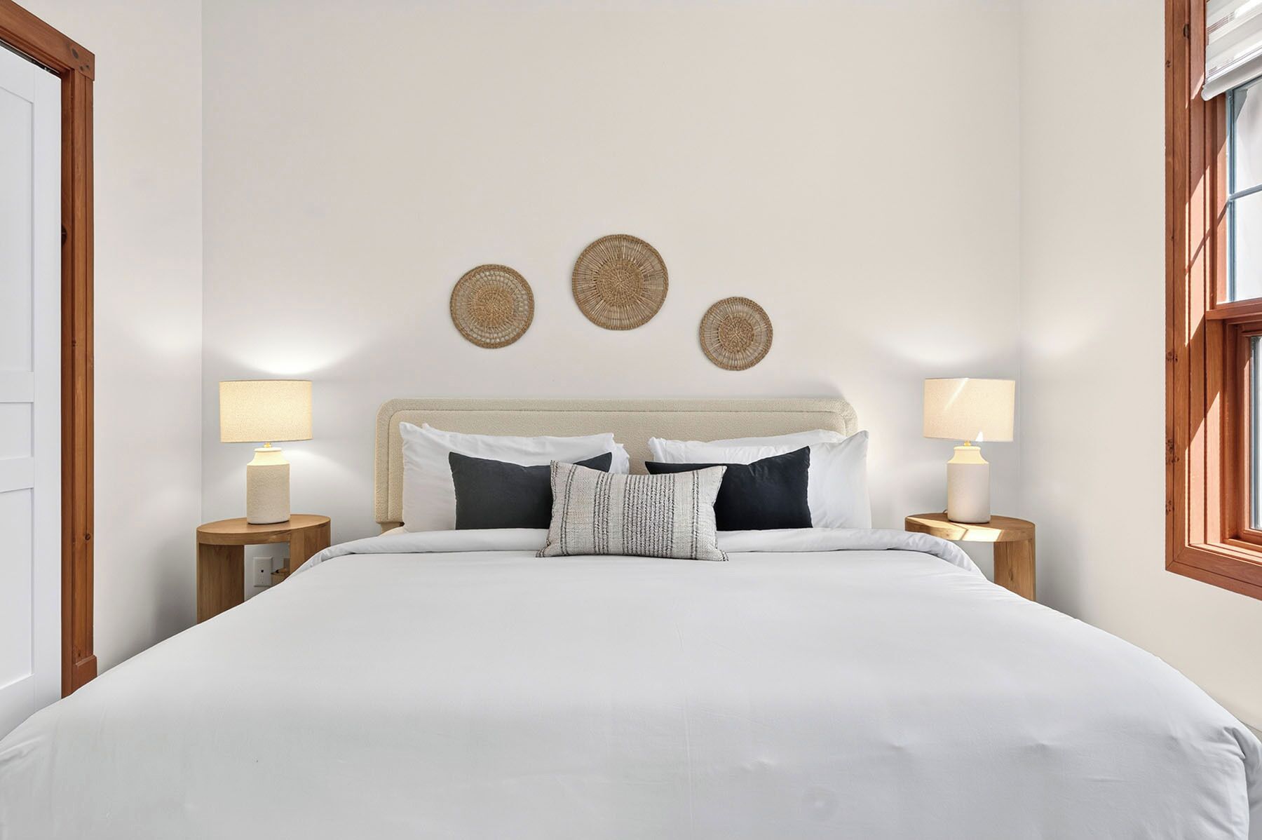 A neatly made bed with white bedding, two bedside lamps, and three woven wall decorations.