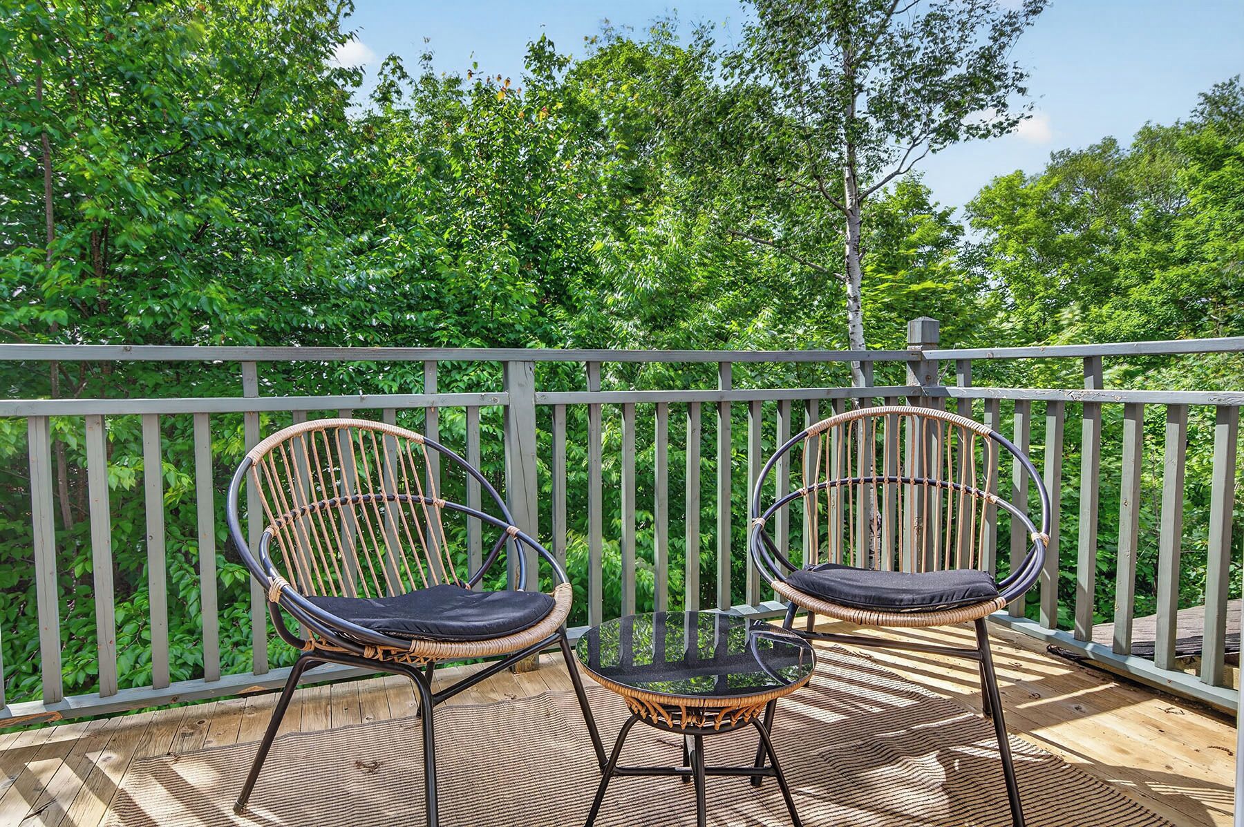 Two wicker chairs with cushions on a wooden deck, overlooking a lush green forest.