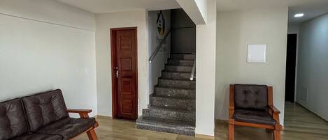 A spacious living area with a wooden coffee table, a sofa, and a chair. A staircase with a handrail leads to an upper floor.