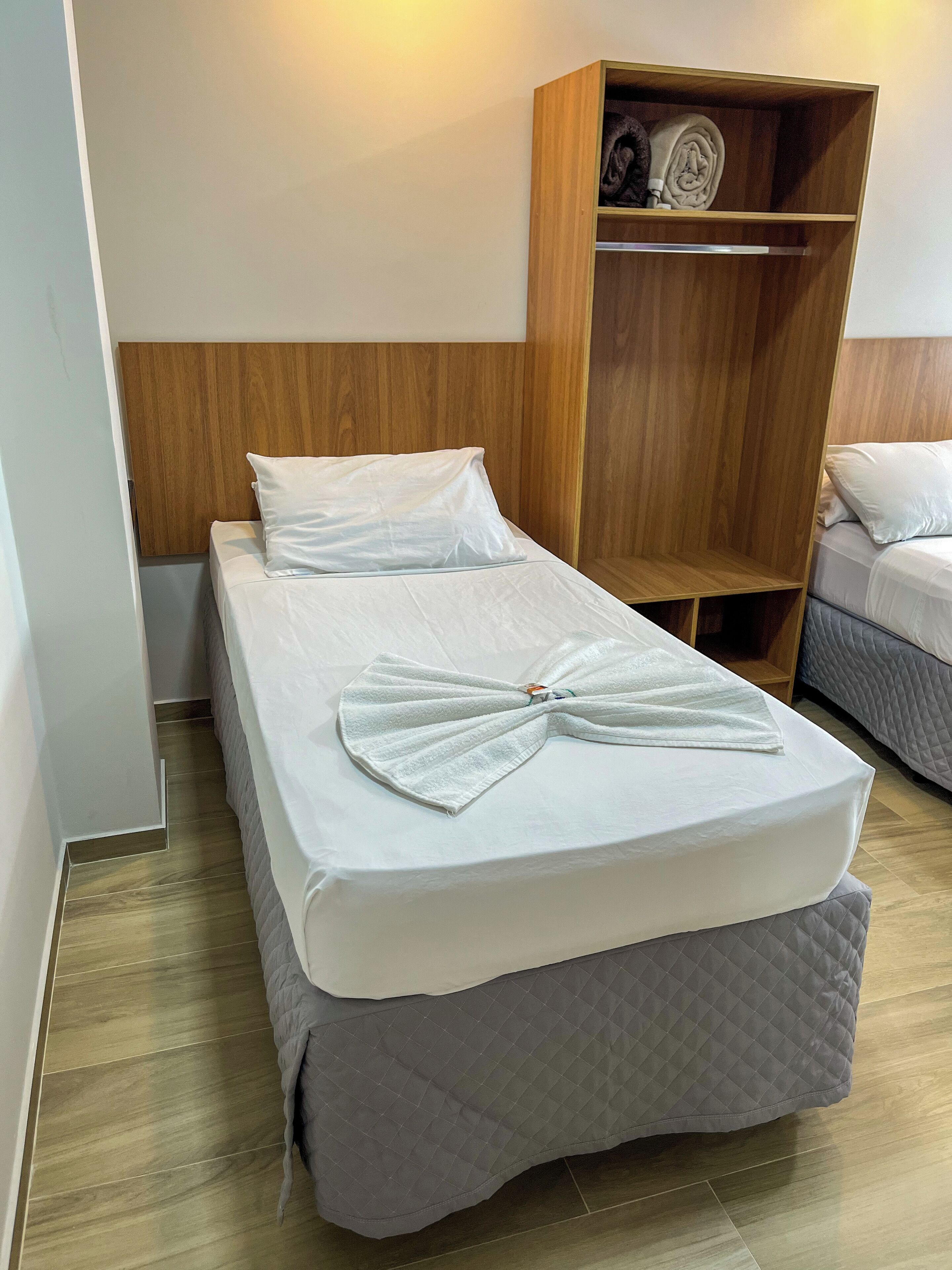 Una habitación de hotel con una cama individual, un armario de madera y otra cama al fondo.