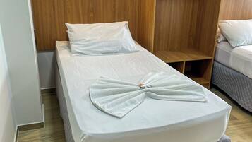 Una habitación de hotel con una cama individual, un armario de madera y otra cama al fondo.