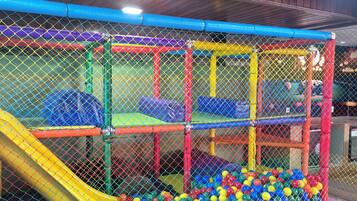 Espaço de recreação com escorrega e piscina de bolinhas, cercado por uma rede.