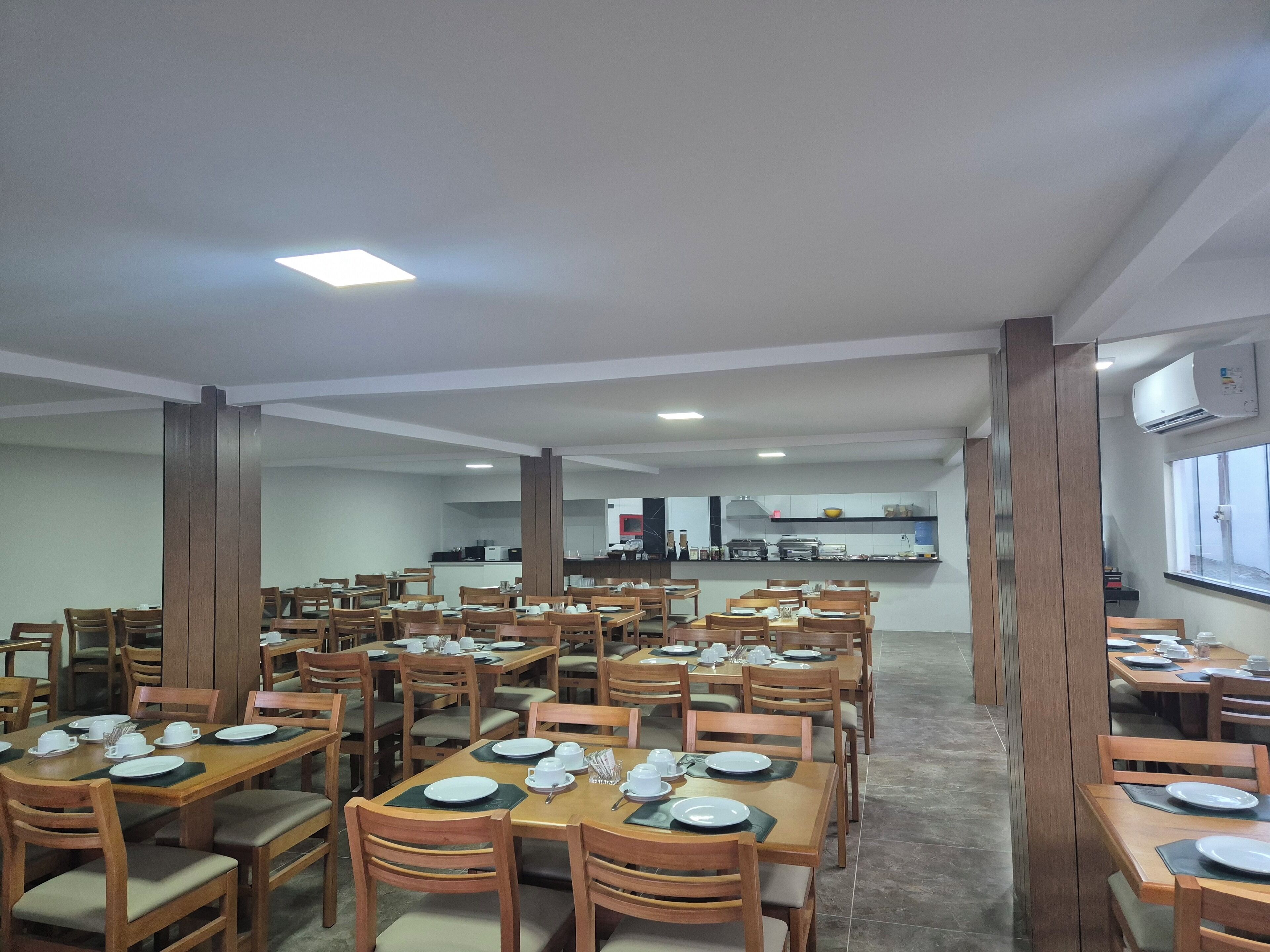 Un comedor amplio con varias mesas y sillas, una cocina al fondo y un equipo de aire acondicionado en la pared.