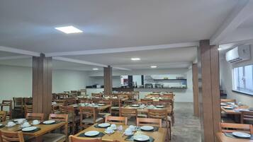 Un comedor amplio con varias mesas y sillas, una cocina al fondo y un equipo de aire acondicionado en la pared.