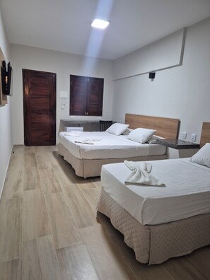 A hotel room with two beds, a wooden door, a large mirror, and a small kitchenette.
