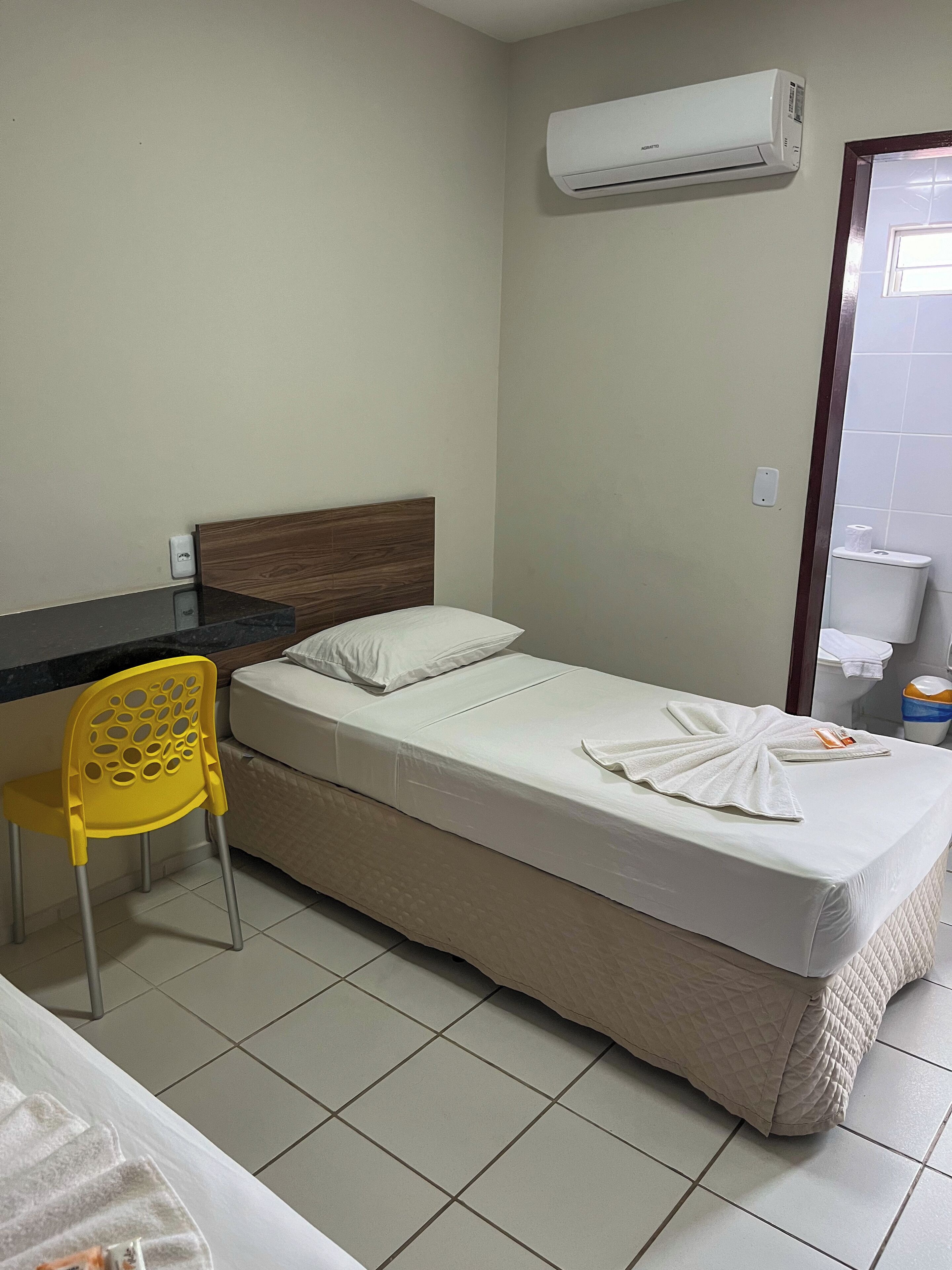 A hotel room with a bed, a desk, a chair, an air conditioner, and a bathroom.