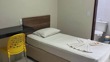A hotel room with a bed, a desk, a chair, an air conditioner, and a bathroom.
