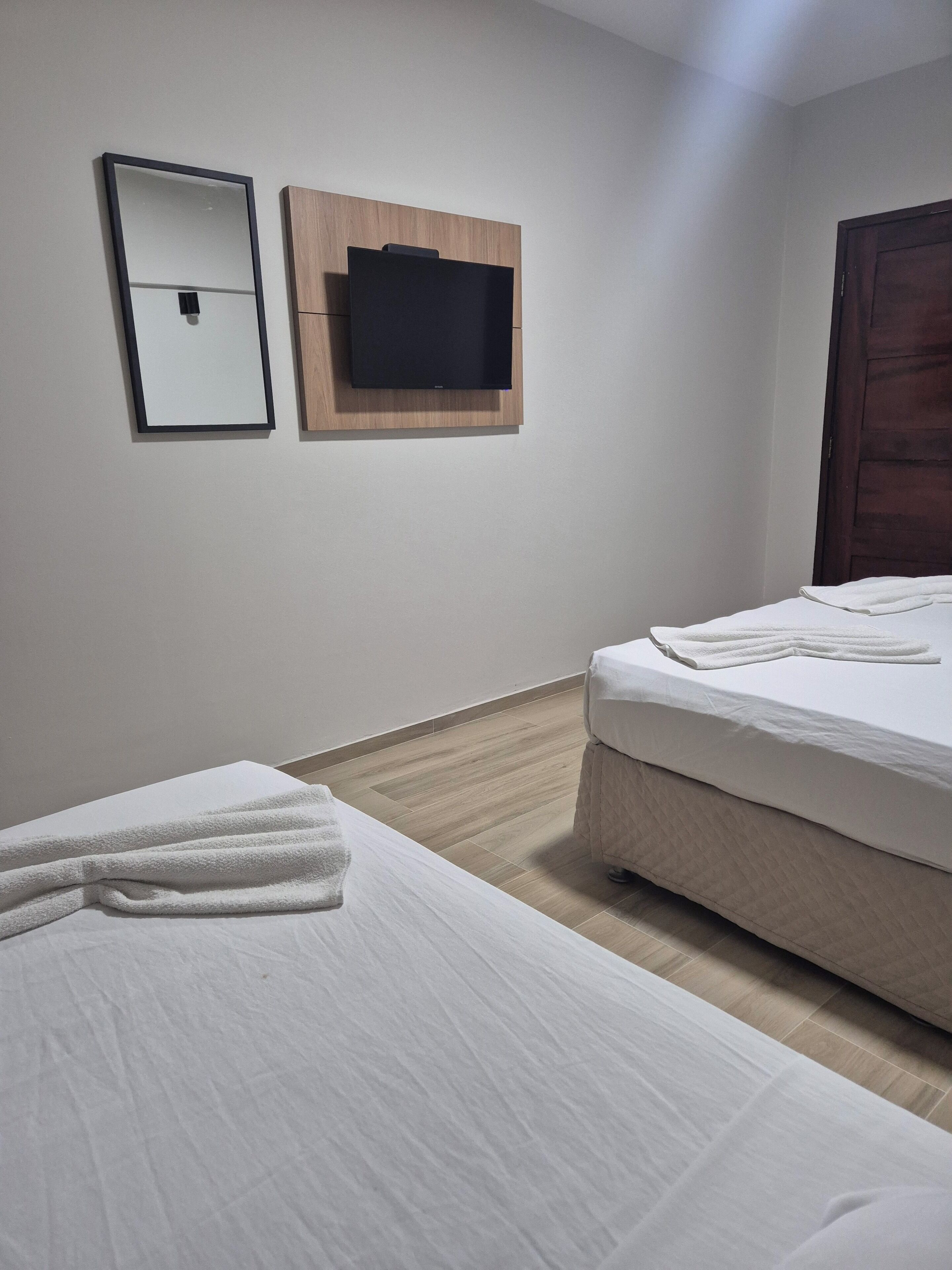 Habitación de hotel con dos camas, un televisor de pantalla plana montado en un panel de madera, un espejo y una puerta de madera.