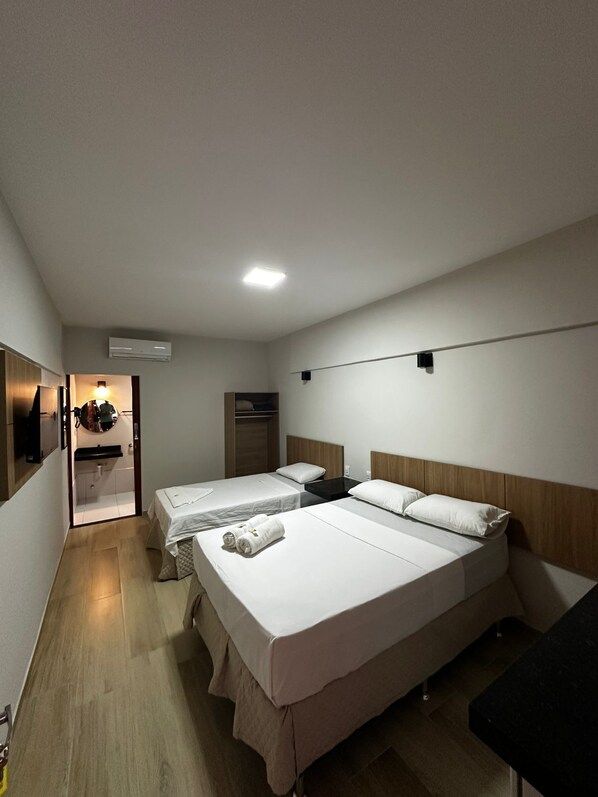 A hotel room with two beds, a small bathroom, and a TV.