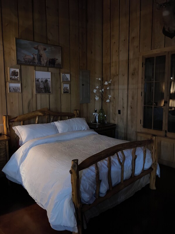 A wooden-paneled room with a large bed, framed pictures on the wall, and a window with curtains.
