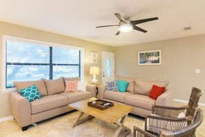 A living room with two beige sofas, a wooden coffee table, and a ceiling fan. - Pure Relaxation: heated pool, beach, cabana & more (St. Augustine)